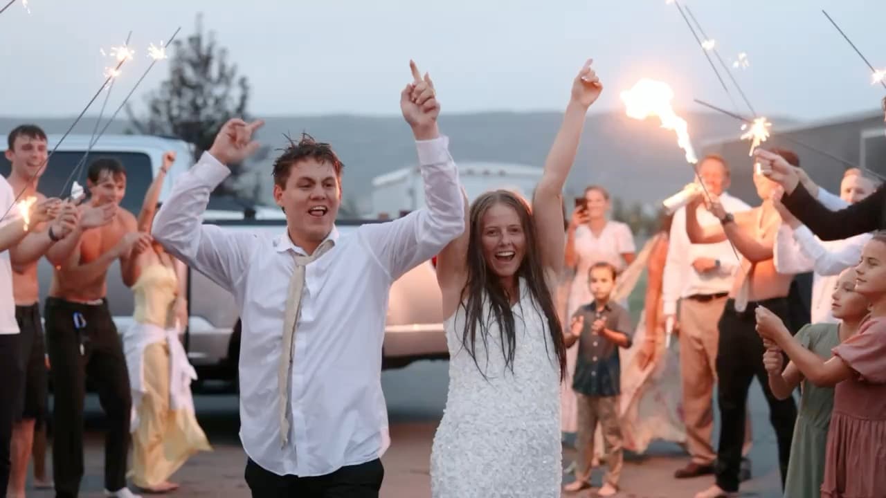 A couple walking out through an arch of sparklers at dusk