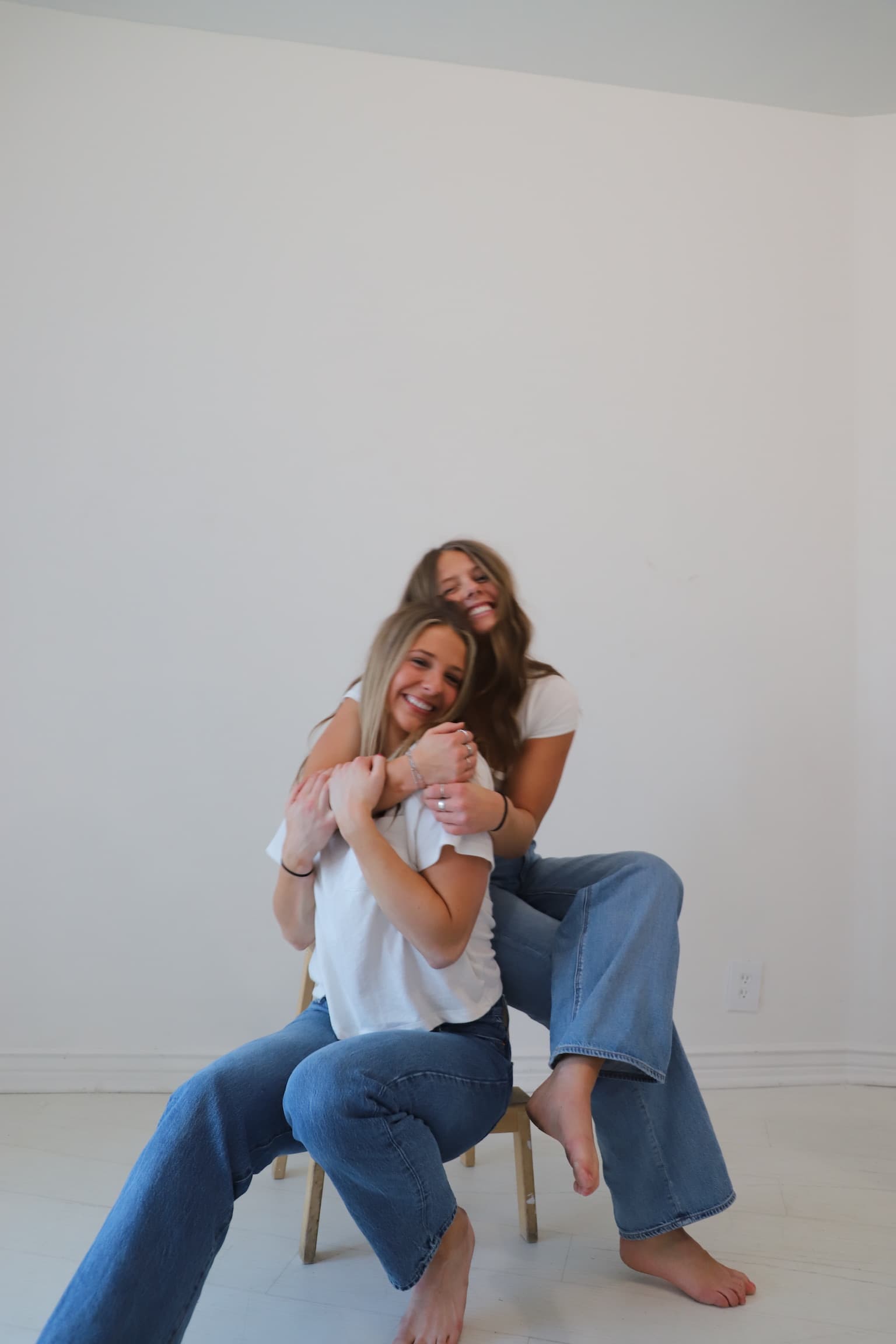 Lexi and Maddy laughing together on a stool in the studio